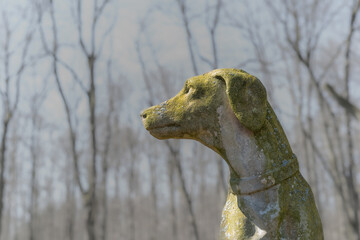 stone statue of hunting dog in front of trees