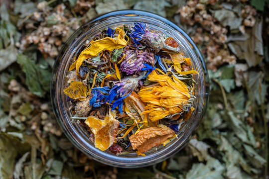Dry flower and herbal tea leaves in a glass jar. Herbal collection of chamomile, cornflower, mint, sea buckthorn, lemongrass, wild rose, dried citrus fruits and apple