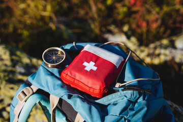Compass first aid kit are in a backpack, a navigator in the taiga, a first aid kit in emergency situations, a white cross, medicines in a red bag. - obrazy, fototapety, plakaty