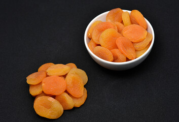 Dried peaches. Delicious dried apricots in ceramic bowls on a black background.