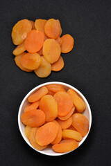Dried peaches. Delicious dried apricots in ceramic bowls on a black background.