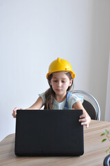 criança brincando de engenheiro com capacete e computador portatil trabalhanco em casa, conceito de sonhar com profissão do futuro 