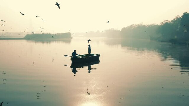 Aerial view of a boat sailing along the Yamuna river at sunset surrounded by seagulls along the coast in New Delhi, India.