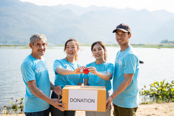 Happy Team of volunteers holding red heart, showing object at camera, smiling. Team promoting charity, donation campaign, health insurance, medical checkup.