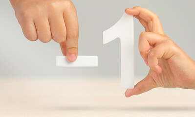 Minus one. The number one and the minus symbol in a hand close-up on a light gray background. The...