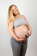 A pregnant girl measures her stomach with a tape-line. Tracking the growth progress of the abdomen and baby.