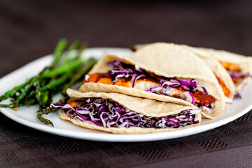 Fish tacos with asparagus on a white plate with brown background