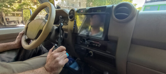 man is holding a walkie-talkie to talk between the crews on the background of road. The driver drives the SUV car at the same time. Adult male with walkie talkie in hand sitting in Off road machine. © Maxim Chuev