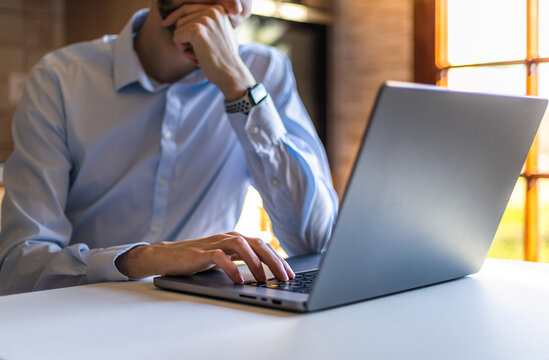 Businessman thinking deeply and working on his laptop at the office. Clean office setup. Typing on keyboard in a modern high tech environment. Technology working from home concept