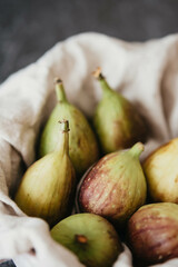 Low-angle view of a basket covered with natural linen with whole figs inside against dark background