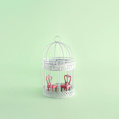 Two chairs in a birdcage, minimal creative relationship concept, pastel green background. 