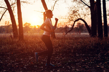 Young female runner training in autumn park. Woman working out with water bottle at sunset. Active lifestyle. Silhouette