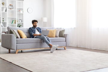 Handsome indian man working on laptop while sitting on couch at home