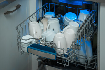 Unclean white cups is loading in steel box of washing machine at home kitchen closeup