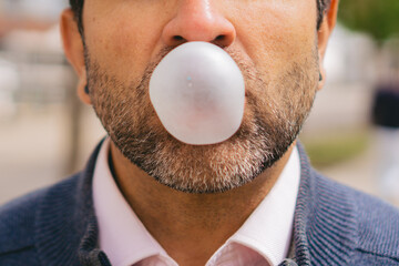 Close-up detail of a bubble made of chewing gum by a middle-aged Latin man with a slightly graying beard.