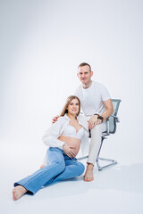 A pregnant woman and a man are standing on a white background. Beautiful young attractive pregnant woman. Family, marriage, childbirth concept. Happy pregnant couple