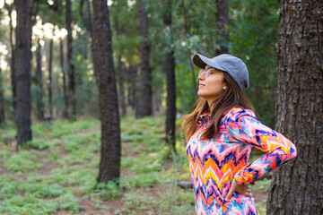 latina woman with multicolored cap and sports jacket breathing relaxed in a forest