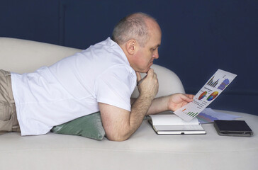A businessman lies on a couch and looks at data trends on charts and graphs.