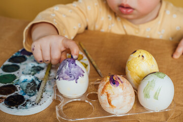 A cute child paints easter eggs with colors.