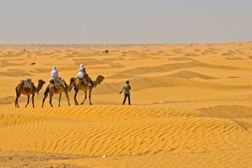 Guide leading two travelers on camels in the Sahara Desert in Tunisia