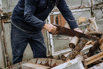 A man in a robe, a lumberjack, a worker saws a tree, a log with a hand saw, outdoors, in nature, at a sawmill. Photo, close-up.