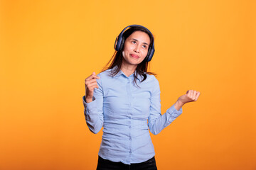 Confident asian woman listening music and dancing, enjoying break time in studio over yellow background. Smiling model wearing headphones showing funny dance moves. Entertainment concept