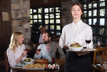 Fototapeta na wymiar Positive woman waiter demonstrating country restaurant to visitors. High quality photo