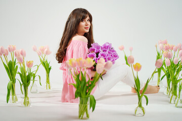 beautiful brunette woman with long hair sits on the floor with vases of flowers 