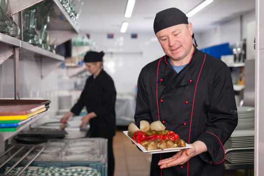 Smiling chef presenting delicious cooked dish in restaurant kitchen, ready to serve it to guests