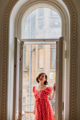 a beautiful and happy brunette women in red retro dress in the balcony doorway 
