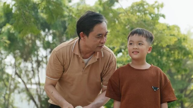 Medium shot of Asian father teaching son how to play badminton during summer day in park