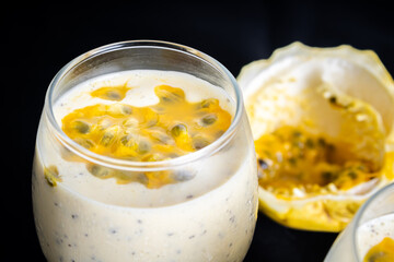 Passion fruit mousse in a glass bowl, with passion fruit in the background, on a black background.