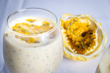 Passion fruit mousse in a glass bowl, with passion fruit in the background, on a white background.