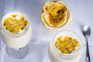 Passion fruit mousse in a glass bowl, with passion fruit in the background, on a white background.