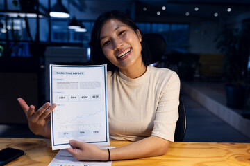 Happy asian businesswoman holding documents making video call, working late at office