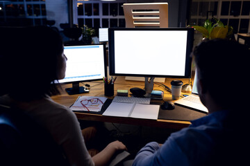Diverse business people at desk, using computers with copy space on screens, working late at office
