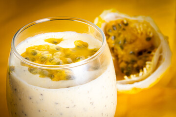 Passion fruit mousse in a glass bowl, with passion fruit in the background, on a yellow background.
