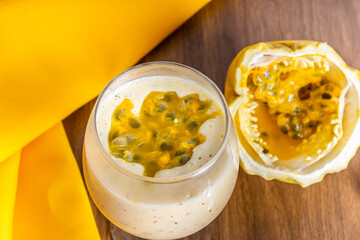 Passion fruit mousse in a glass bowl, with passion fruit in the background, on a wooden table and a yellow tablecloth around it.