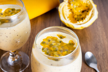 Passion fruit mousse in a glass bowl, with passion fruit in the background, on a wooden table and a yellow tablecloth around it.