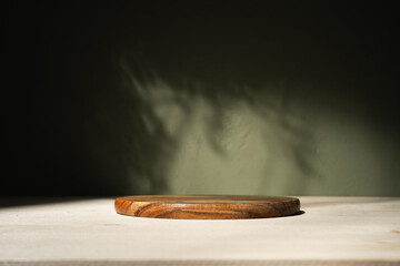 Round wooden podium for food, products or cosmetics against khaki wall with shadows and sun...
