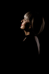 Beautiful girl with blond bangs fringe against black background. Abstract sidelit portrait. .