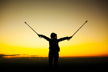 Silhouette of a hiker girl on a rock pedestal with hands up. Beautiful orange sunset.