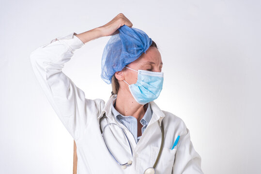 Una mujer con mascarilla y estetoscopio se quita la cofia de la cabeza, cansada, doctora
