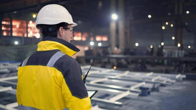 A male process engineer works on a personal computer. Portrait of a professional heavy industry engineer. Building under construction. Safety glasses and hard hat. 4K slow motion