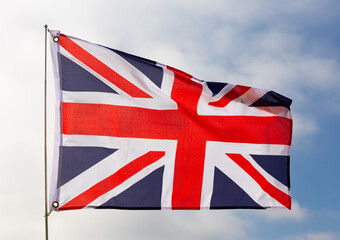 Against background of cloudy sky, cloth fabric flag flutters of United Kingdom of Great Britain and Northern Ireland flutters on flagpole.Isolated