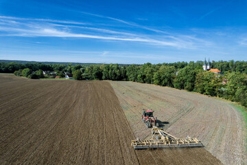 large crawler tractor mills the ground in a field near the village. Top view of field work using modern technologies.