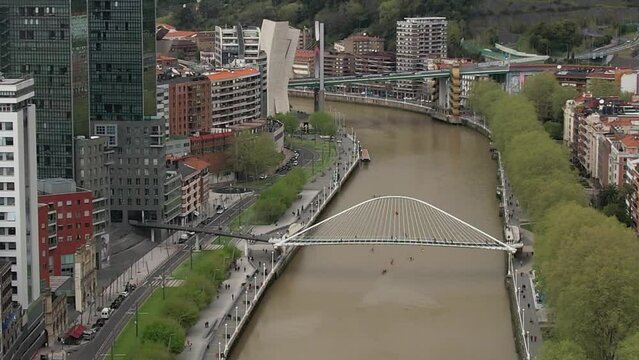 Aerial drone view along the Nervion River in Bilbao, Basque Country, Spain towards the Zubizuri bridge