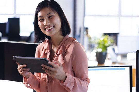 Portrait of happy asian businesswoman smiling, holding tablet, working late at office