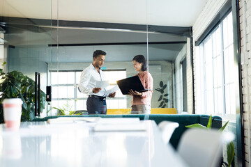 Diverse business people using laptop, holding documents and discussing, working late at office