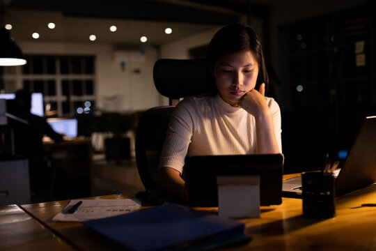 Asian businesswoman sitting at desk and using tablet, working late at office